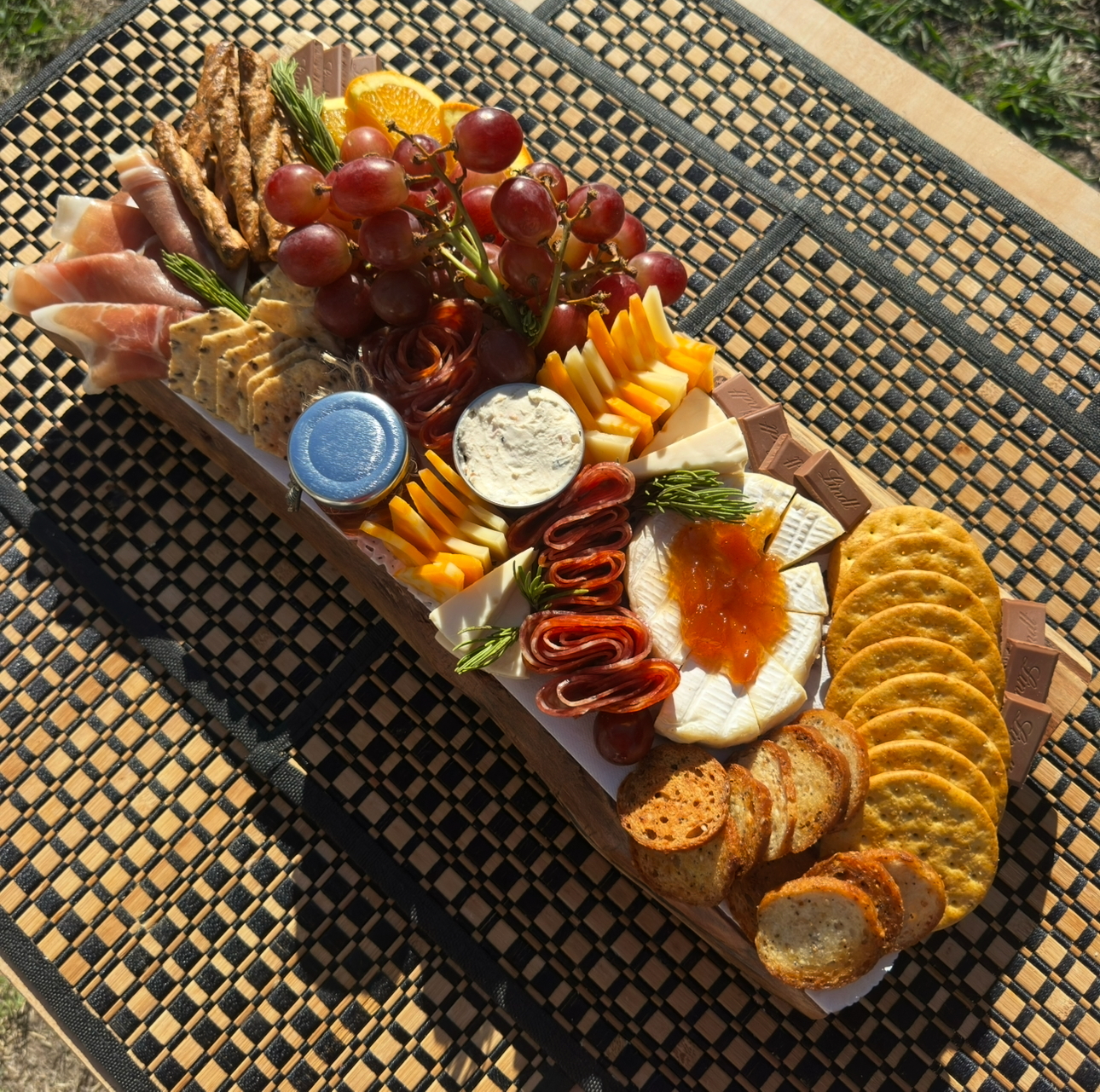 Assorted charcuterie board with meats, cheeses, and crackers on a woven mat.