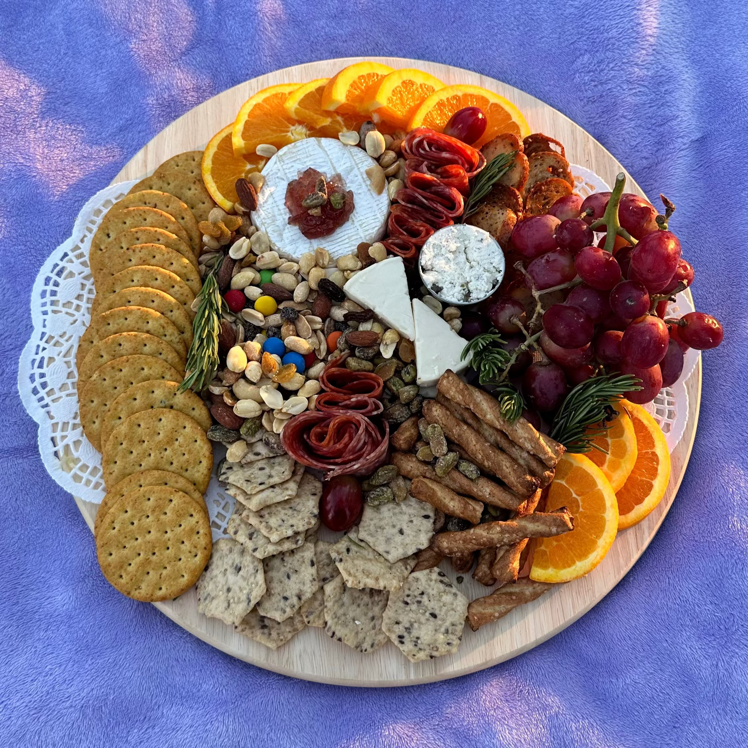 Assorted food platter with fruits, cheese, and crackers on a purple textured surface